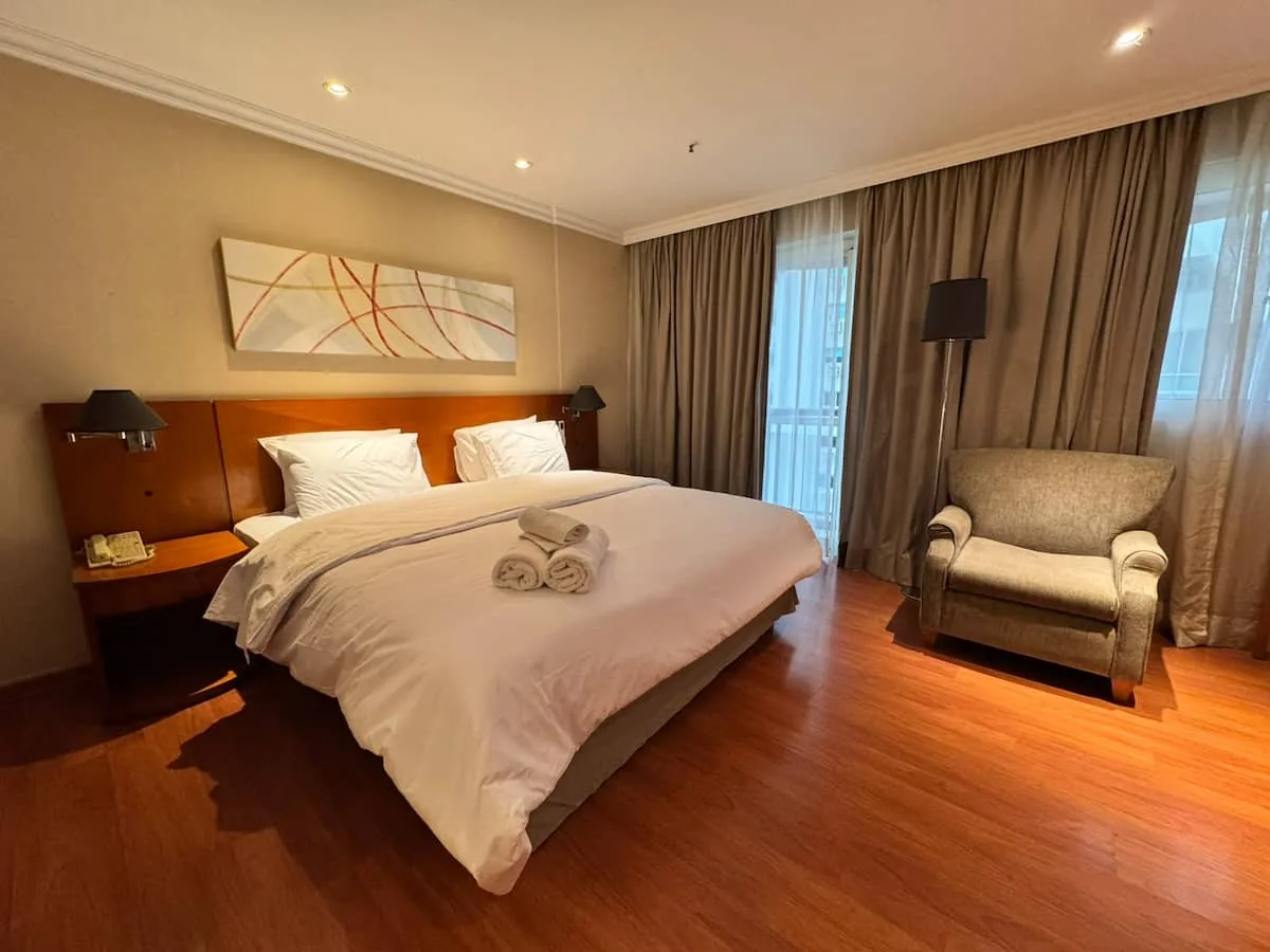 Cama king com roupa de cama branca, poltrona e abajures