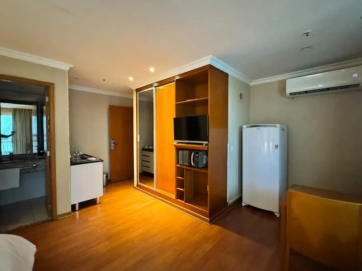 Vista geral do flat com armário de TV, geladeira e ar-condicionado