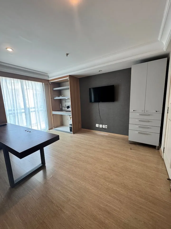 Ambiente com TV de parede, armário e kitchenette